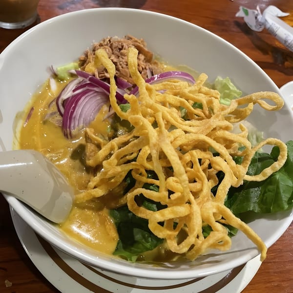 Close-up of a Thai Khao Soi dish with crispy noodles, red onions, and green lettuce.