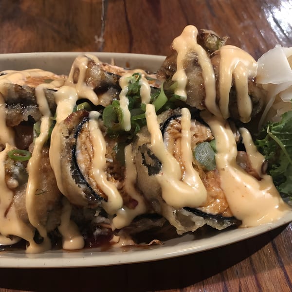 Close-up of deep-fried sushi rolls drizzled with creamy sauce, garnished with scallions and pickled ginger.