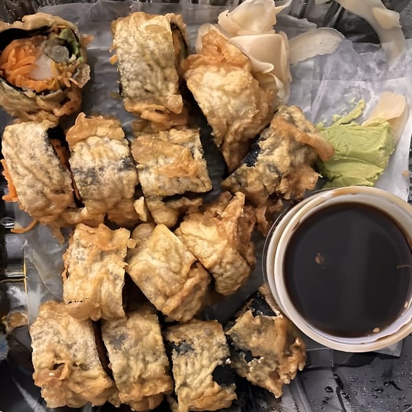 Tempura-fried sushi rolls with soy sauce, wasabi, and pickled ginger in a takeout container.